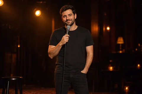 A stand-up performer holding a microphone on a warmly lit stage